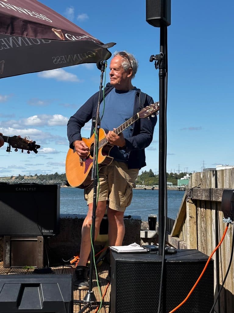 Steve Patten playing acoustic guitar by the water