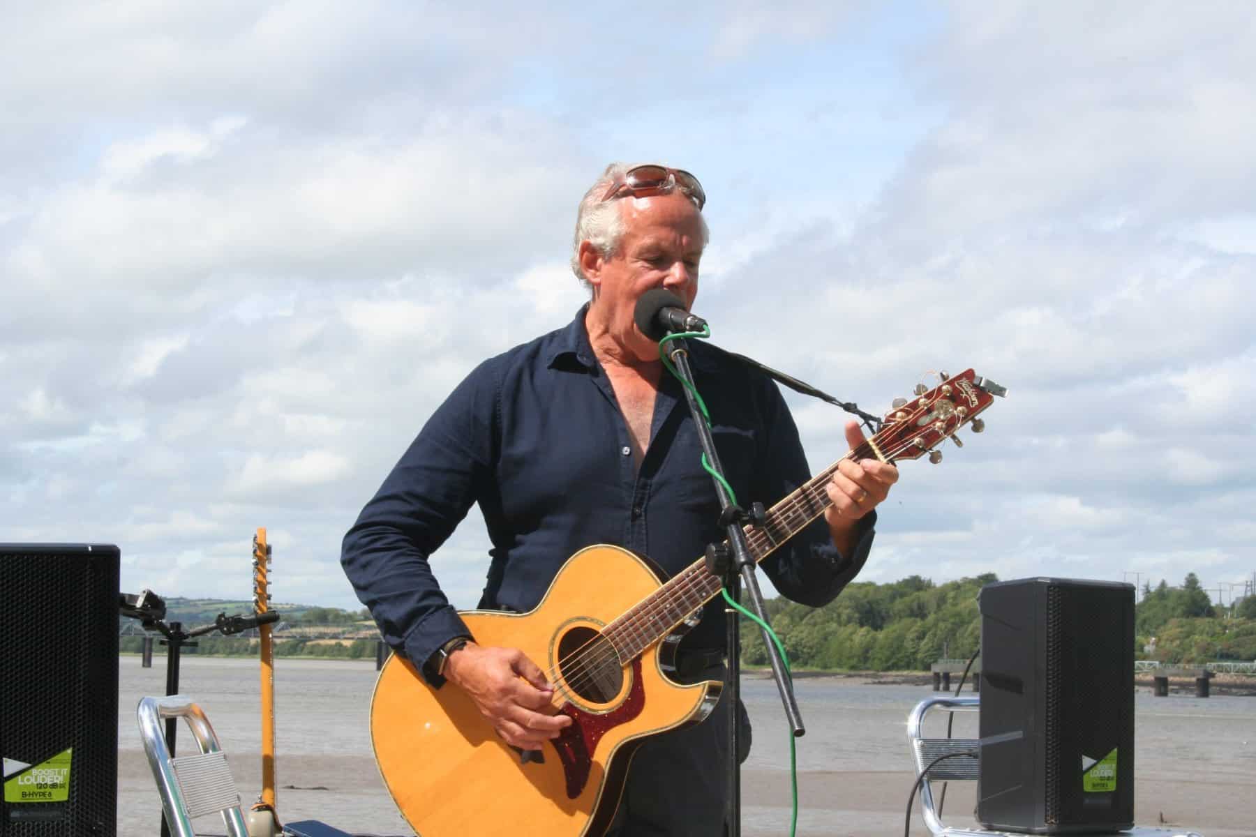 Steve Patten singing with an acoustic guitar by the river at the Suir Inn, Cheekpoint